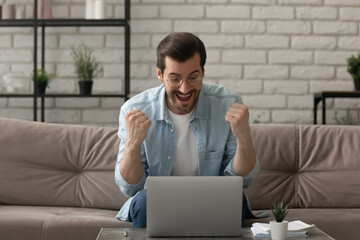 Great thing. Euphoric young man sit on couch by laptop screen shout super raise fists in winner gesture get good news job offer email. Amazed excited funny guy celebrate victory in web game of chance