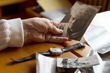 An Old Watch Next To An Old Woman's Hand. Next To Old Photos. Memories, Nostalgia, Time Concept