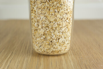 View of rolled oats inside a plastic jar that is on top of a wooden table with the background of white tiles