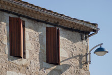 Detail Of A Sandstone Building. Two Windows With Open Window Shutters.  Lantern Fixed To The Wall.