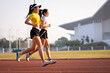 © EduLife Photos - Two young Asian women in sports outfits jogging on running track in city stadium in the sunny morning to keep fitness and healthy lifestyle. Young women run on the stadium track. Sports and recreation