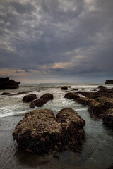 Wall Mural - Amazing seascape for background. Beach with rocks and stones. Low tide. Motion water. Cloudy sky. Slow shutter speed. Soft focus. Mengening beach, Bali