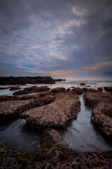 Wall Mural - Amazing seascape for background. Beach with rocks and stones. Low tide. Motion water. Cloudy sky. Slow shutter speed. Soft focus. Mengening beach, Bali