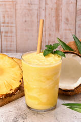 pineapple coconut smoothie with a bamboo straw and a mint leaf on top. on the side pineapple slices and two coconuts. stone surface and white wooden planks background. copy space for advertising.