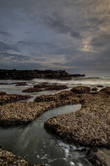 Wall Mural - Beautiful seascape for background. Beach with rocks and stones. Low tide. Motion water. Cloudy sky. Slow shutter speed. Soft focus. Copy space. Vertical layout. Mengening beach, Bali