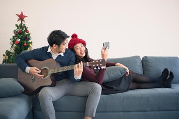 Asian man and woman couple family in casual outfit holiday winter theme live together and playing music guitar with happy and romantic in modern living room