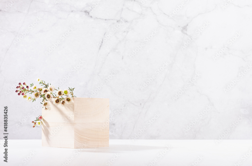 Wooden cube podium with twig of white spring flowers in white and grey marble interior with sun light and shadow. Showcase for cosmetics, products. - obrazy, fototapety, plakaty 