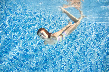 Fototapete - Child swims in swimming pool underwater, happy active girl jumps, dives and has fun under water, kids fitness and sport on family vacation
