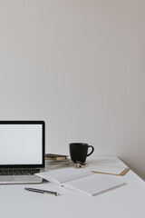 Wall Mural - Laptop with blank copy space mockup screen on table with coffee cup, paper sheet against white wall. Minimalist home office workspace.