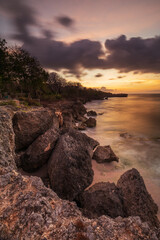 Wall Mural - Sunset view. Seascape background. Amazing ocean view. Beach with rocks and stones. Bright sunlight on horizon line. Cloudy sky. Vertical layout. Bali.