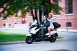 © Kalim - Happy mature couple riding a scooter in the city on a sunny day