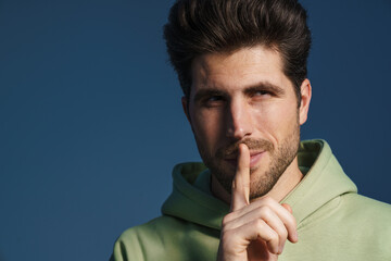 Wall Mural - Pleased handsome man in sportswear showing silence gesture