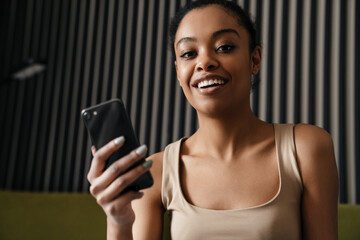 Wall Mural - Happy african american girl smiling while using mobile phone at home