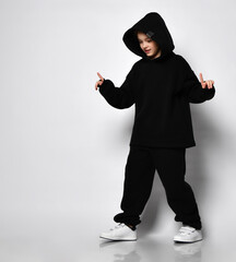 Guy teenager in black hoodie and pants dancing street dance style on isolated light background