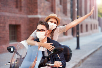 Poster - Happy mature couple wearing masks while riding a scooter in the city on a sunny day