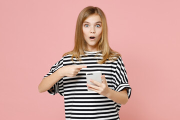 Wall Mural - Little blonde shocked kid girl 12-13 years old wearing striped oversized t-shirt point index finger on mobile cell phone chat isolated on pastel pink background children. Childhood lifestyle concept.