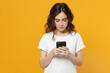 © ViDi Studio - Young happy caucasian student cool woman 20s wear white basic casual t-shirt look camera hold mobile cell phone chatting browsing internet isolated on yellow orange color background studio portrait