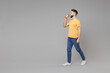 © ViDi Studio - Full length of young bearded attractive smiling student man 20s wearing casual yellow basic t-shirt walking drinking coffee holding paper cup of tea isolated on grey color background studio portrait