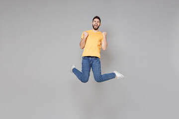 Wall Mural - Full length of young bearded excited successful overjoyed man 20s in yellow basic t-shirt walk doing winner gesture clenching fist jump high celebrating isolated on grey background studio portrait