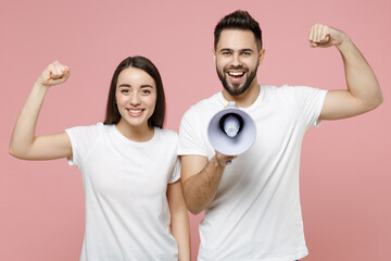 Wall Mural - Young fun couple two friends man woman in white basic blank print design t-shirts hold scream in megaphone announces discounts sale Hurry up isolated on pastel pink color background studio portrait.