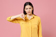 Young brunette cute nice sad bored dissatisfied displeased latin student woman 20s wearing yellow casual shirt show thumb up dislike gesture isolated on pastel pink color background studio portrait.