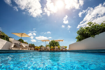 Loungers placed on the left and in the front of a pool with clean looking water on a sunny day.