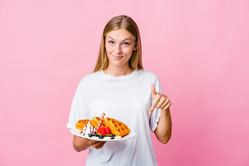 Wall Mural - Young russian woman eating a waffle isolated points down with fingers, positive feeling.