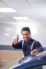 Wall Mural - car mechanic standing next to a serviced car and showing thumbs up before delivery	