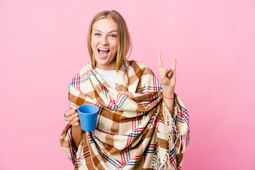 Canvas Print - Young russian woman wrapped in a blanket drinking coffee showing a horns gesture as a revolution concept.