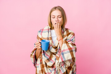 Canvas Print - Young russian woman wrapped in a blanket drinking coffee yawning showing a tired gesture covering mouth with hand.