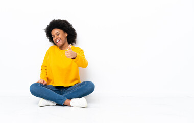 young african american woman sitting on the floor with thumbs up because something good has happened