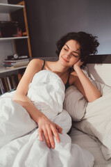 Wall Mural - Woman lying in white bed on pillows under blanket, resting head on hands