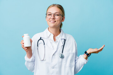 Wall Mural - Young russian doctor woman holding pills bottle on blue showing a welcome expression.