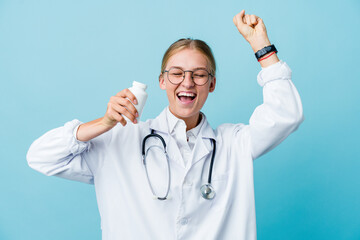 Wall Mural - Young russian doctor woman holding pills bottle on blue celebrating a special day, jumps and raise arms with energy.