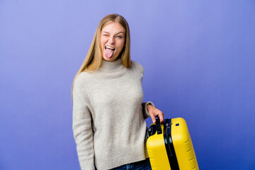 Wall Mural - Young russian woman holding suitcase to travel funny and friendly sticking out tongue.