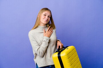 Wall Mural - Young russian woman holding suitcase to travel has friendly expression, pressing palm to chest. Love concept.