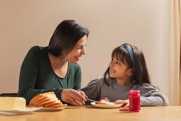 A HAPPY MOTHER LOOKING AT DAUGHTER WHILE SPREADING JAM ON A SLICE OF BREAD	