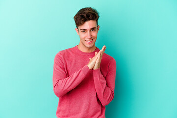 Wall Mural - Young caucasian man isolated on blue background feeling energetic and comfortable, rubbing hands confident.