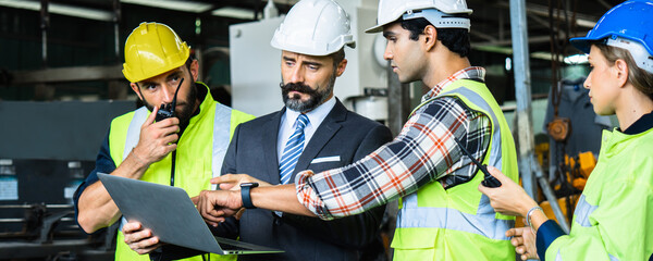 Engineer manager in suite with white helmet checking on laptop order working and planning with engineering team in factory, industry development and technology concept