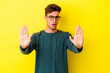 © Asier - Young caucasian man isolated on yellow background standing with outstretched hand showing stop sign, preventing you.