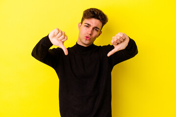 Wall Mural - Young caucasian man isolated on yellow background showing thumb down and expressing dislike.