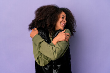 Young african american curly woman isolated on purple background hugs, smiling carefree and happy.