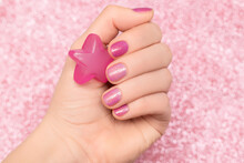 Female Hand With Red Nail Design. Glitter Red Nail Polish Manicure. Woman Hand Hold Red Star On Pink Fabric