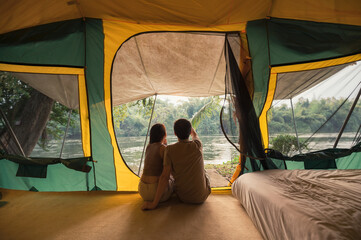 Wall Mural - Young asian couple relaxing inside a tent on campsite in natural park