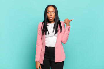 Wall Mural - young black woman looking astonished in disbelief, pointing at object on the side and saying wow, unbelievable. business concept