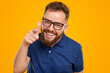Positive bearded man in eyeglasses pointing at camera
