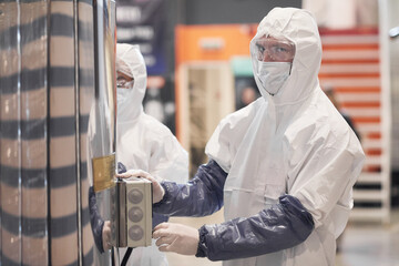 Waist up portrait of male worker wearing protective suit while operating equipment at chemical plant, copy space