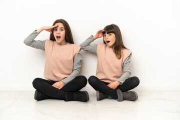 Little sisters sitting on the floor isolated on white background has just realized something and has intending the solution