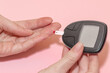 © Rytis - Health care concept. Close-up view of woman fingers doing blood test for sugar level (glucose) with lancet, test strip and meter in pink background with copy-space