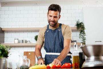 Wall Mural - Handsome man preparing vegetable salad in the kitchen. Healthy Food. Vegan Salad..